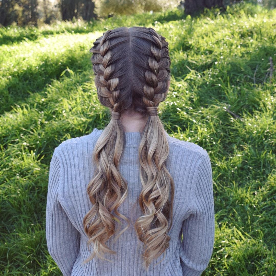 Two French braids ending in long, loose curled pigtails against a green garden