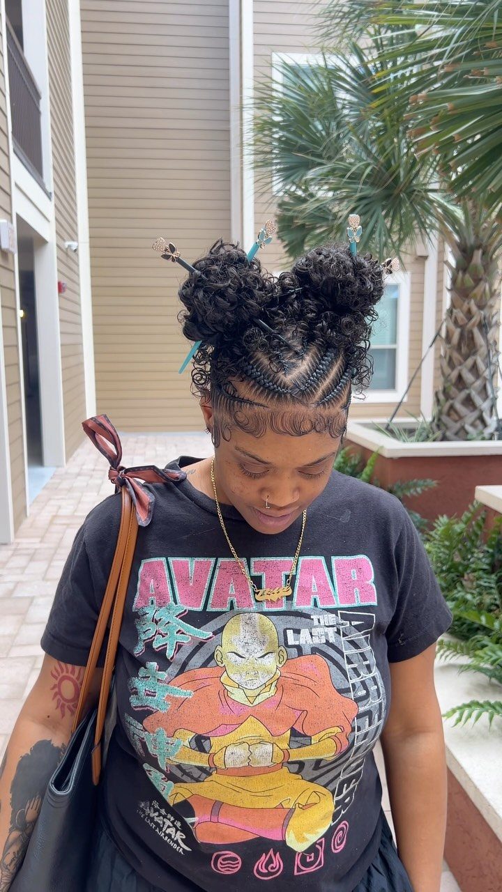 Person wearing two messy braided buns outdoors beside a building and palm trees
