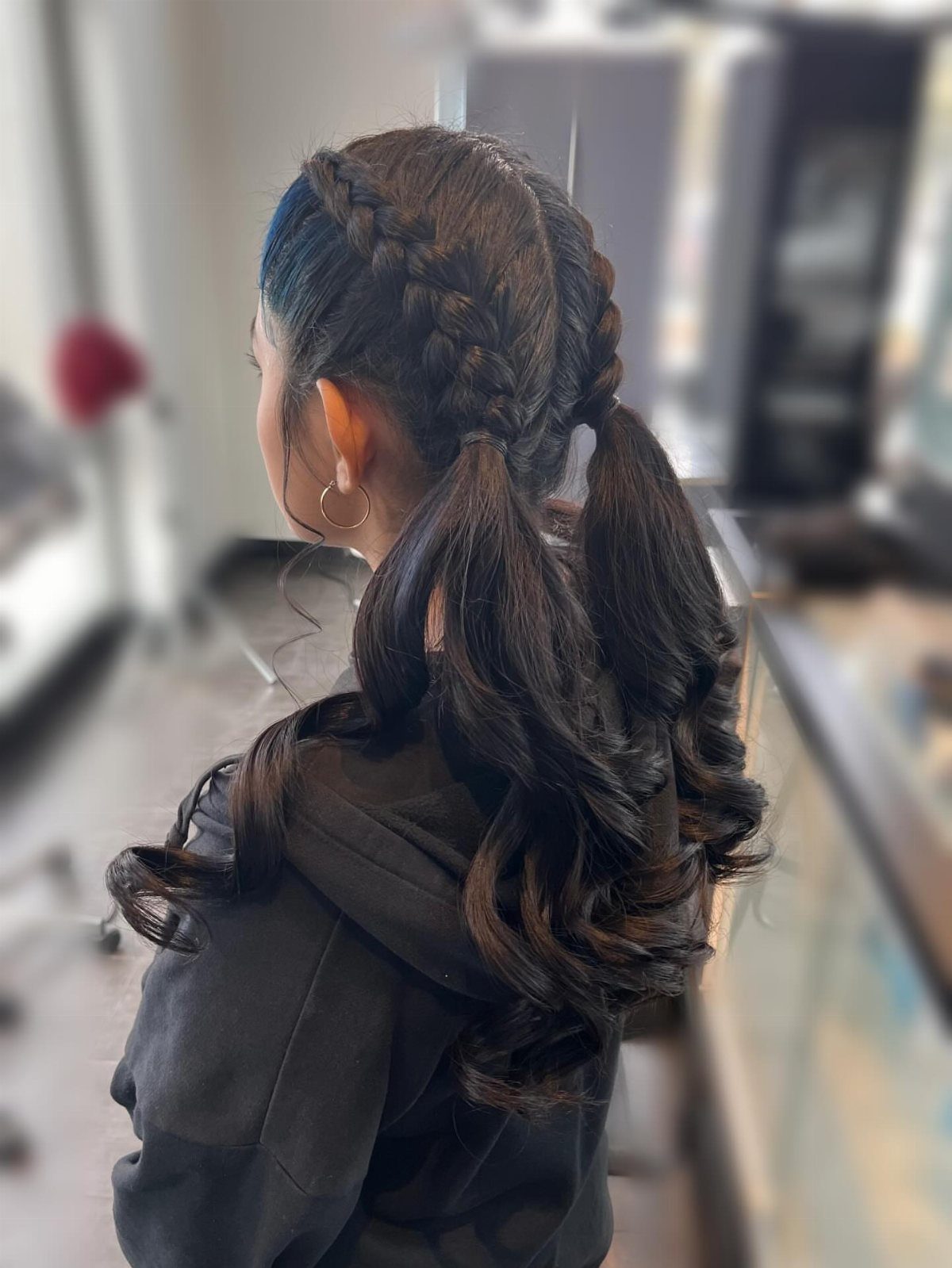 Two thick braids gather into curled low ponytails on dark hair