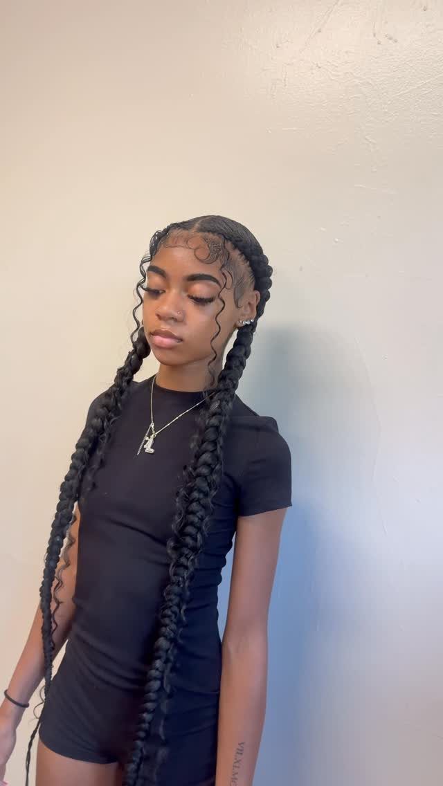 Woman showcasing two long braids with styled edges against a light wall