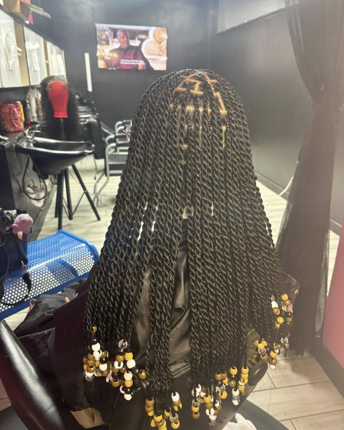 Long black two-strand twists end in yellow and white beads in a salon