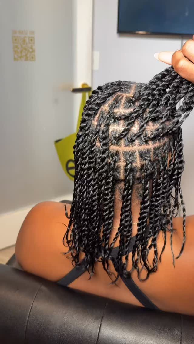 Small black twists hang from square-parted natural hair as a section is lifted