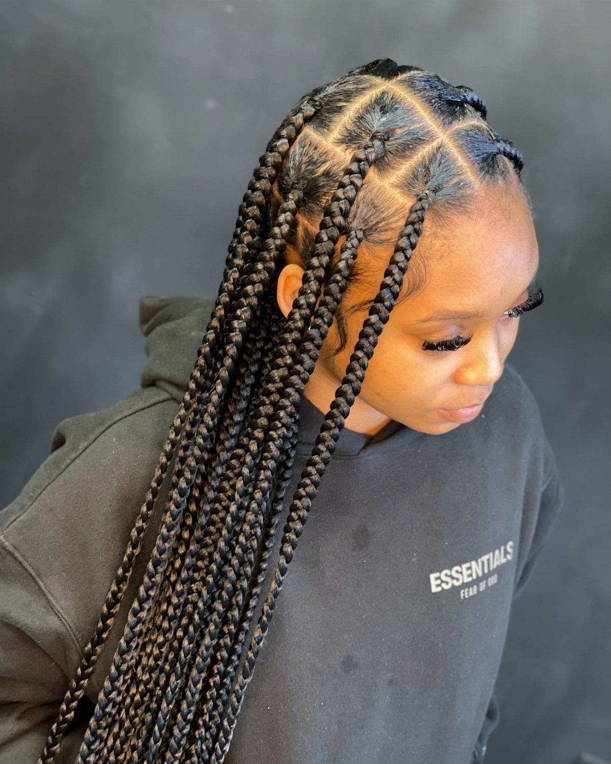 Long individual box braids with square partings drape over a woman's shoulder