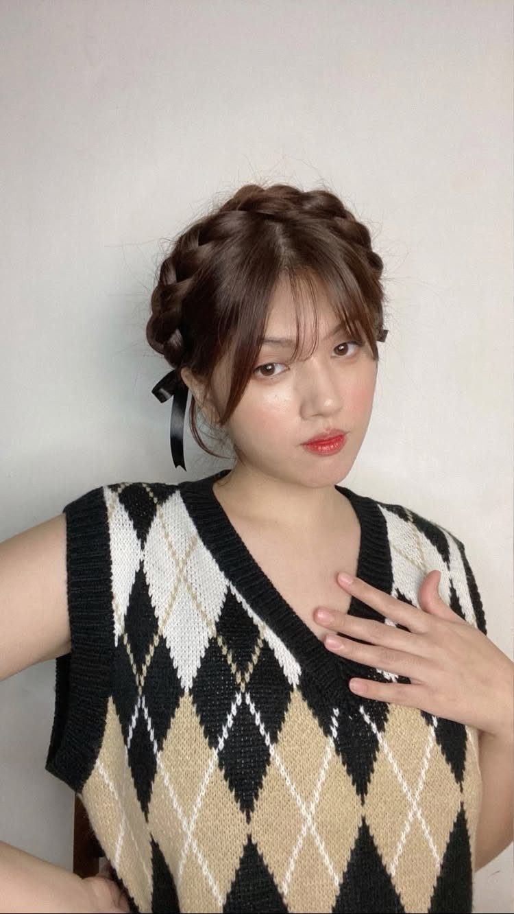 Woman with brown crown braid, loose bangs, and a black ribbon