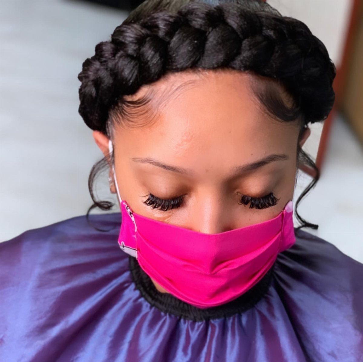 Thick dark halo braid wraps around a person's head above a bright pink mask