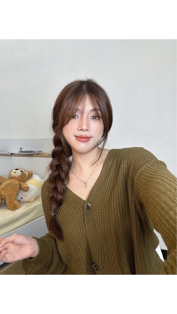 Woman wearing a long brown side braid over one shoulder indoors