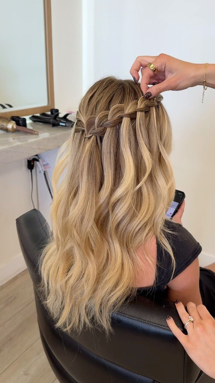 Blonde waterfall braid with loose strands cascading down the back in a salon