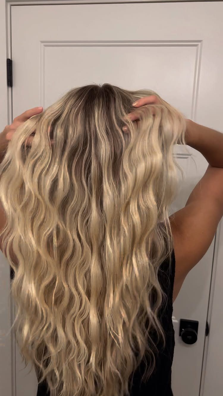 Long blonde hair with dark roots falls in loose, tousled waves