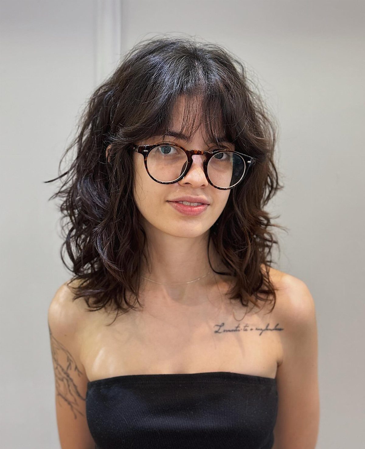 Woman wearing shoulder-length dark wavy hair with choppy layers and bangs