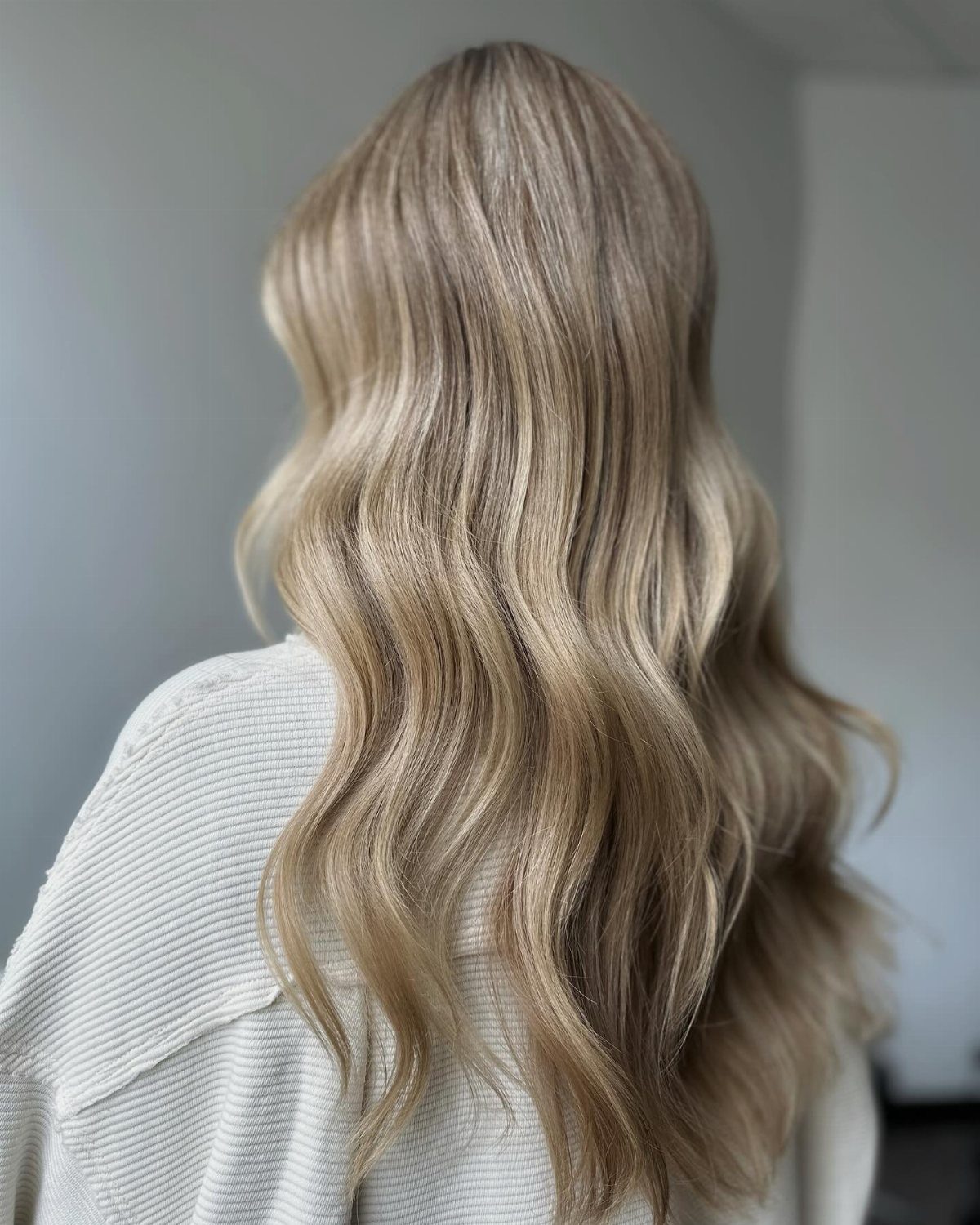 Long blonde hair falls in large, soft waves over a white ribbed top