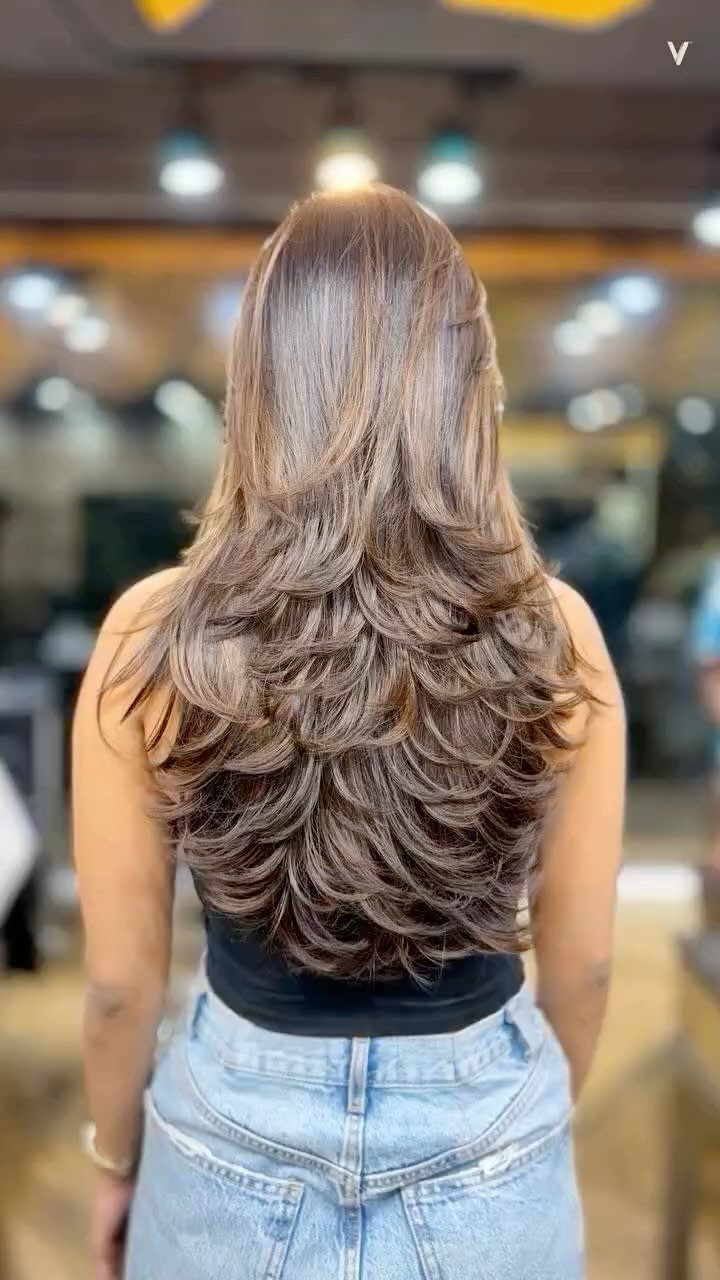 Long brown layered waves cascade down the back above light blue jeans