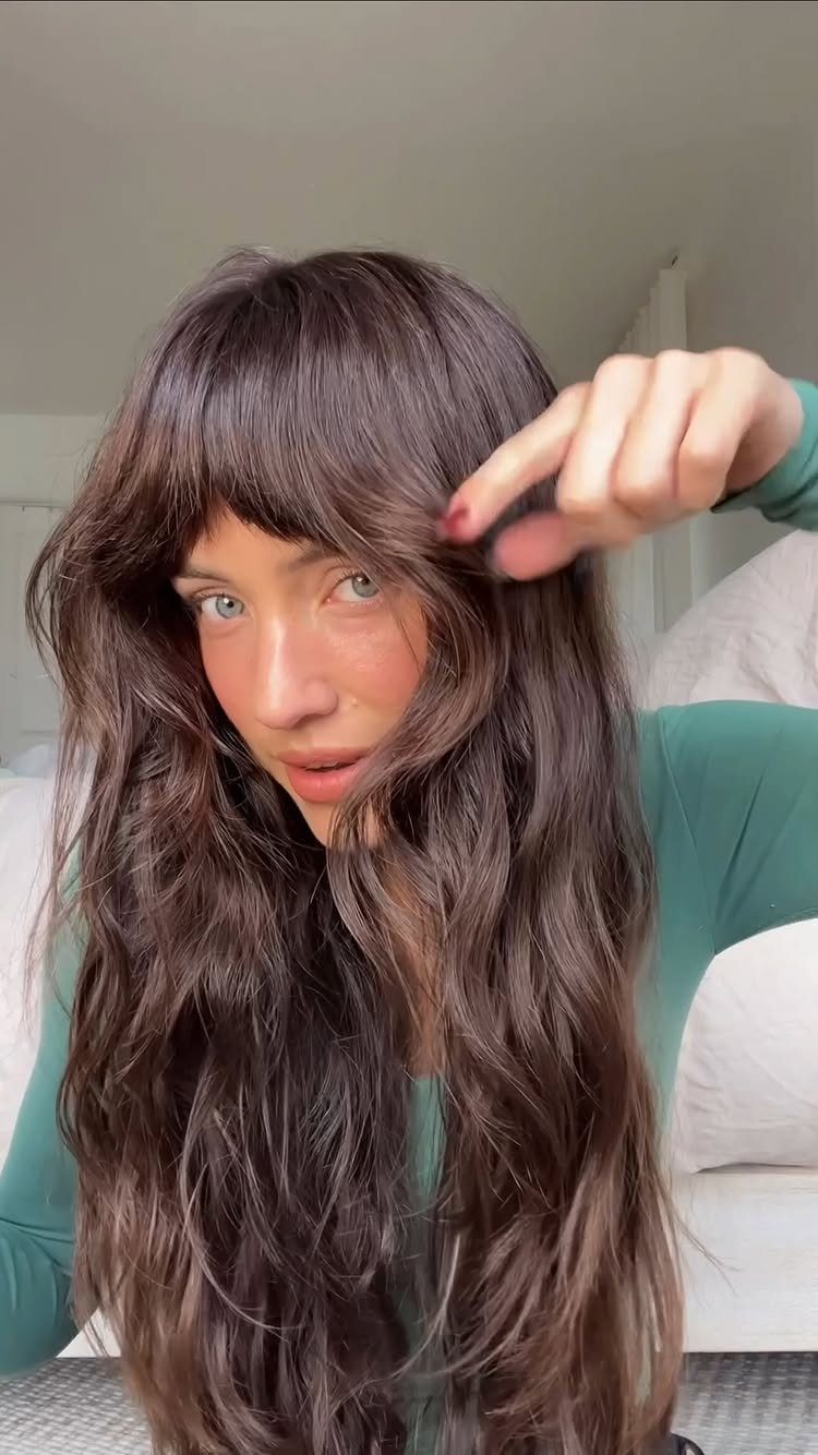 Person points to full bangs above long, dark brown wavy hair