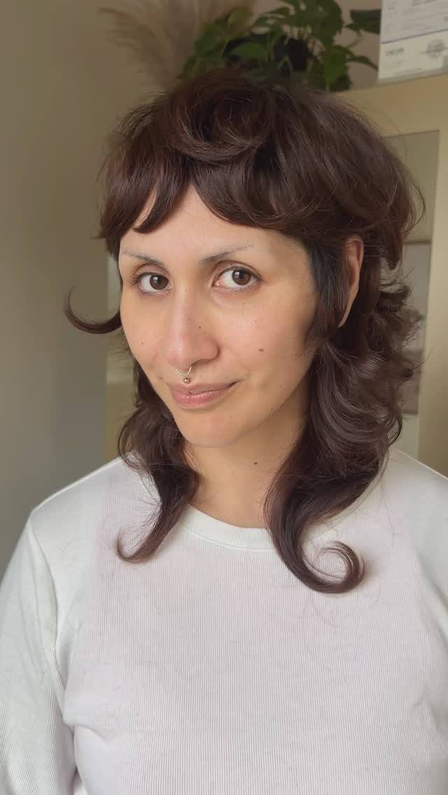 Person showing a dark brown wavy shaggy mullet with short bangs and curled ends
