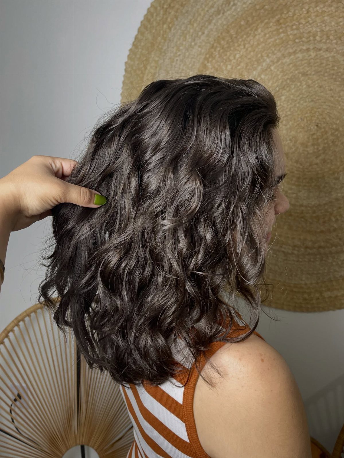 Dark neck-length wavy lob shown from behind as a hand lifts the hair