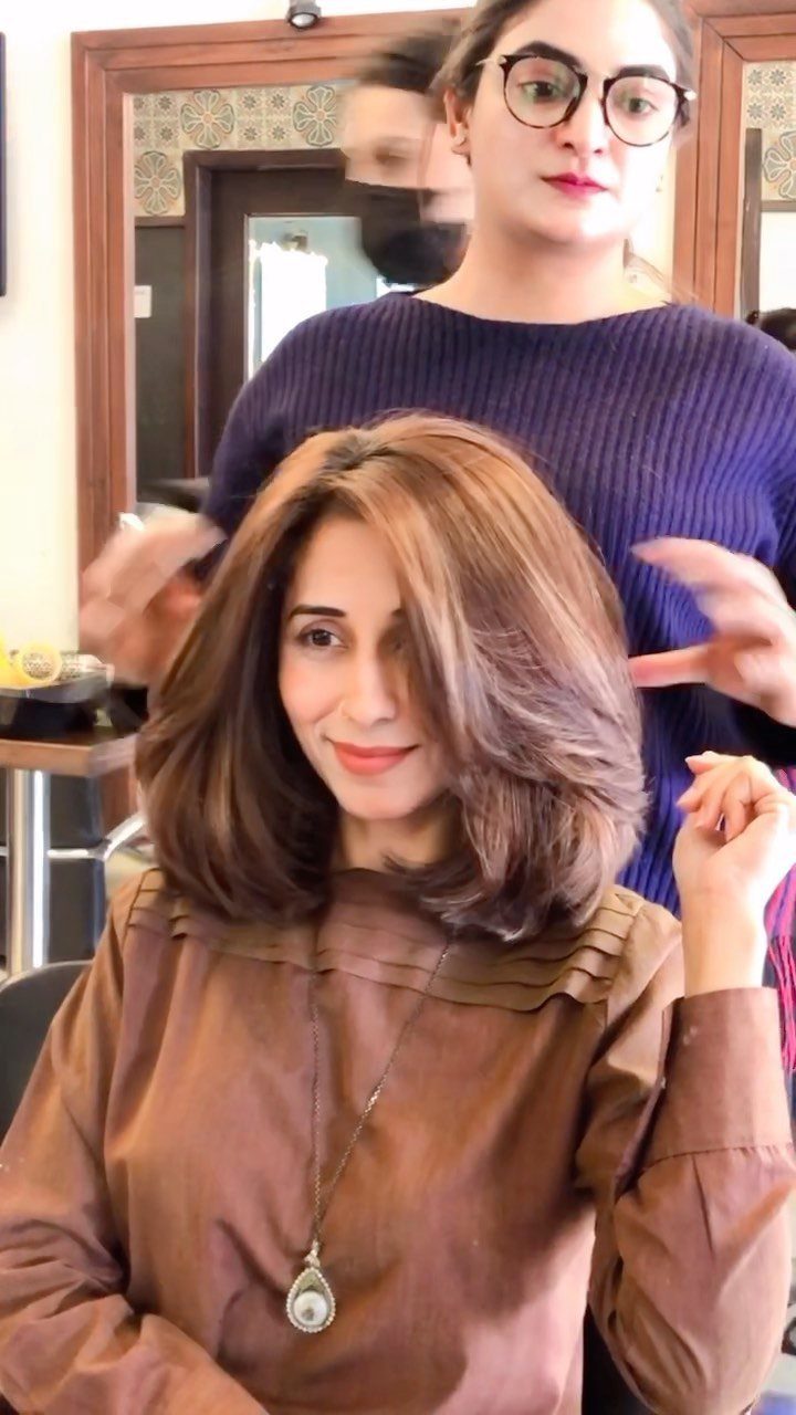 Woman with layered, shoulder-length brown waves seated in a salon chair