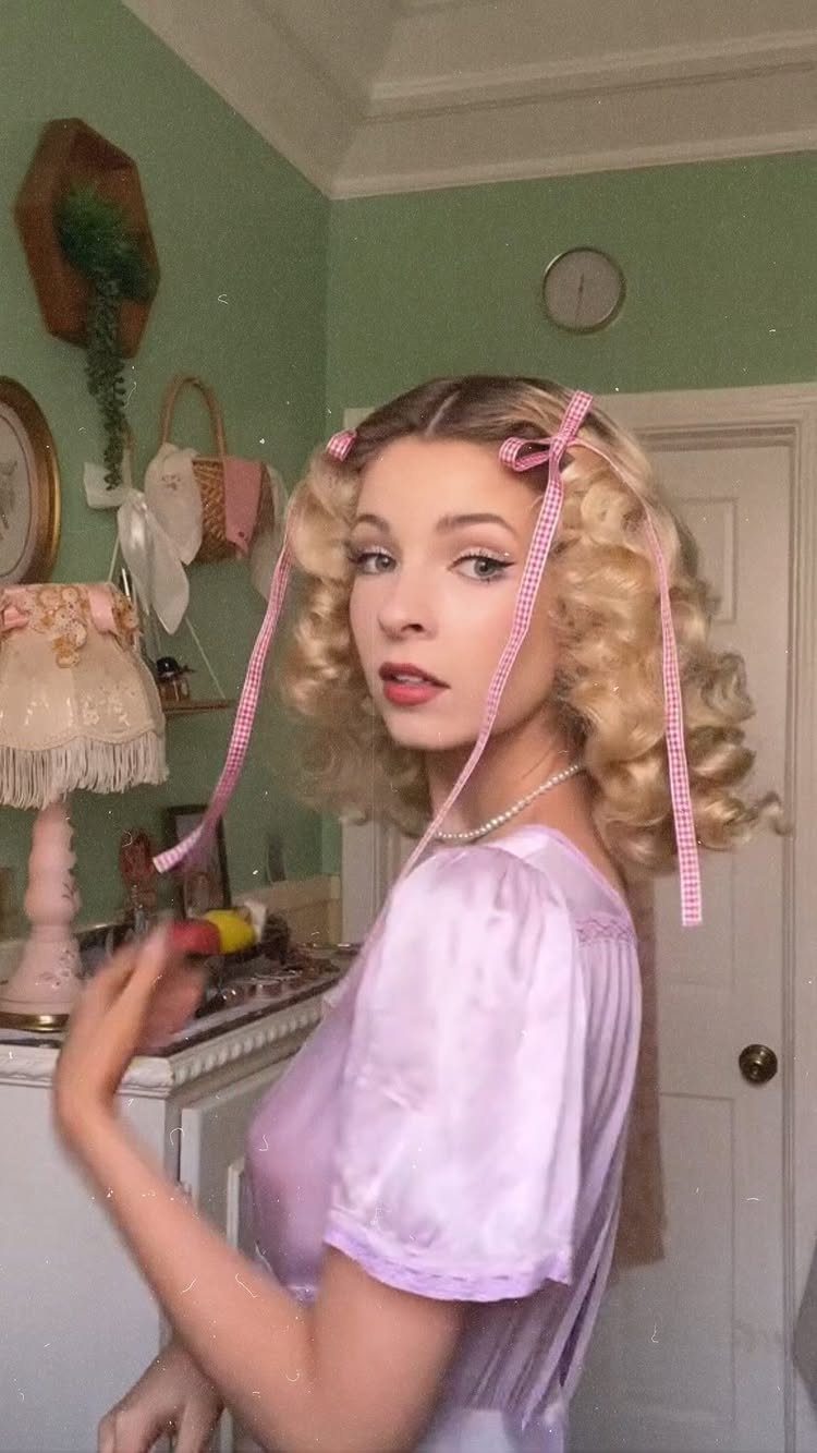 Woman with blonde retro curls and pink ribbons standing in a mint-green room