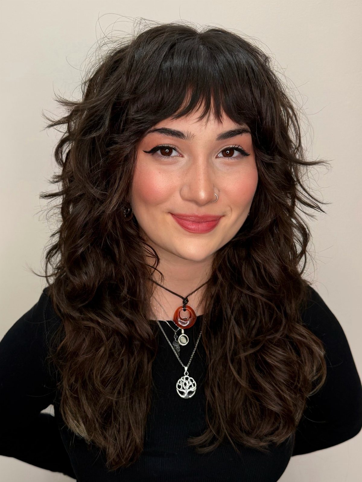 Woman wearing a tousled soft shag haircut with dark wavy layers and wispy bangs