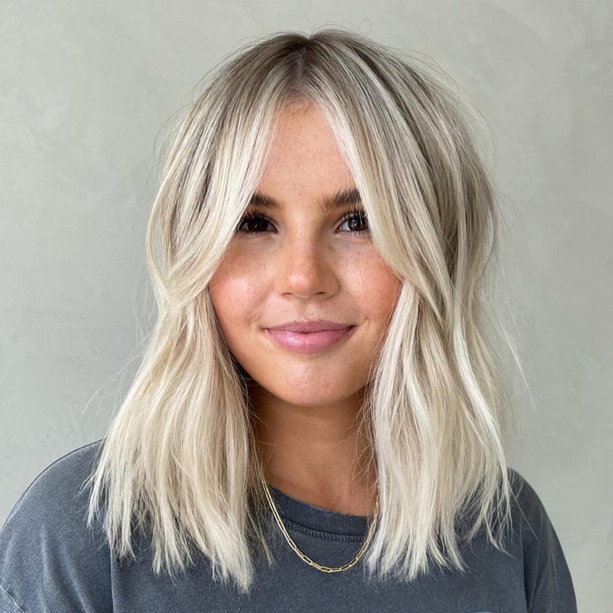 Woman showcasing shoulder-length blonde waves with center-parted curtain bangs