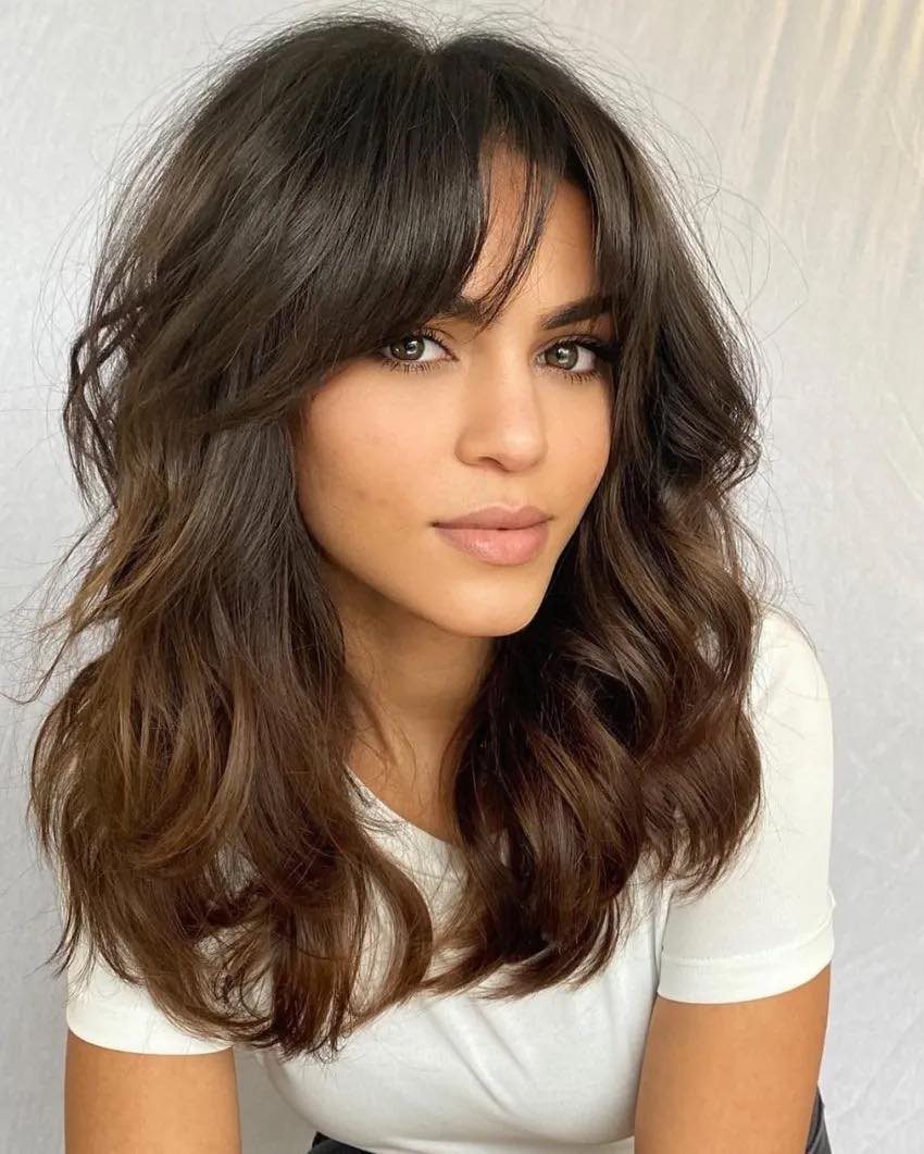 Woman with center-parted curtain bangs blending into long, dark wavy hair