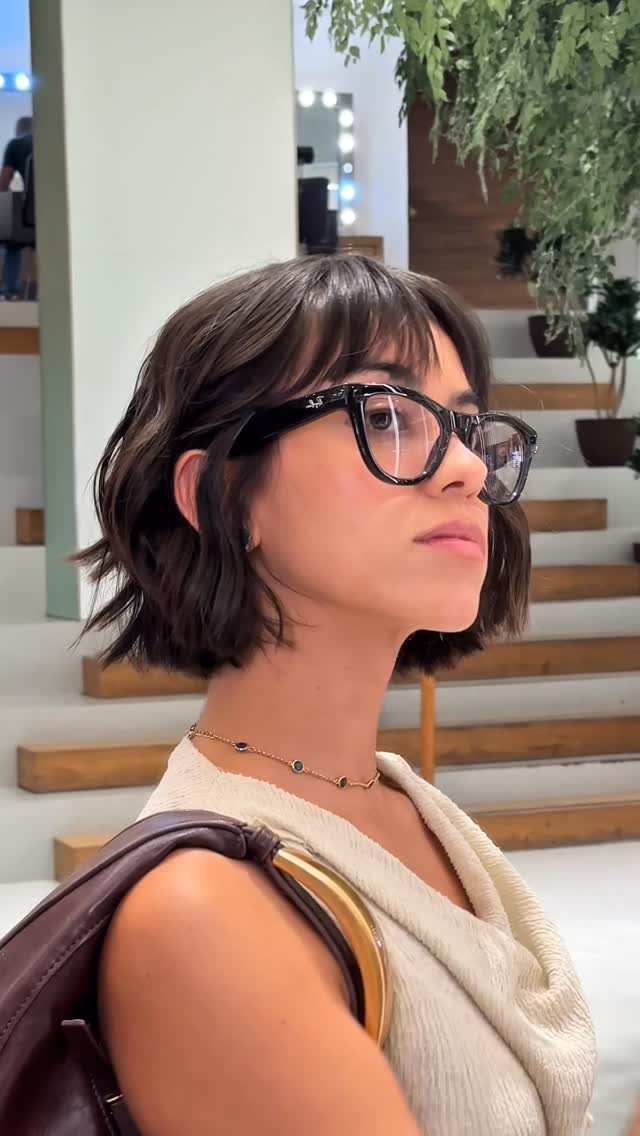 Woman wearing glasses with a short wavy bob and wispy bangs indoors