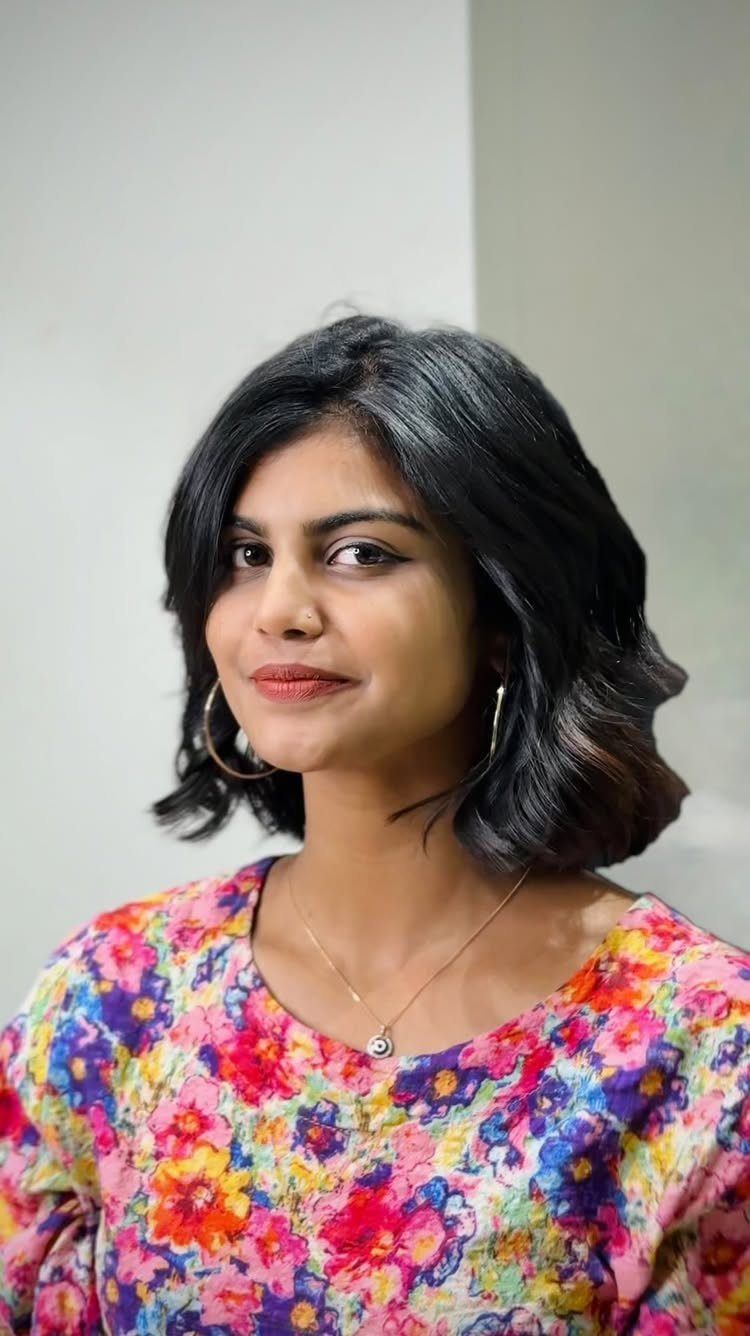 Woman wearing a glossy dark wavy bob with chin-length curls and a floral top