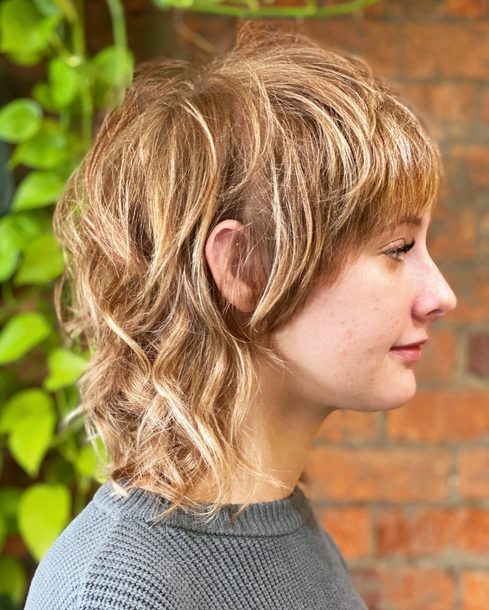 Blonde wavy mullet with short bangs and longer curls at the neck