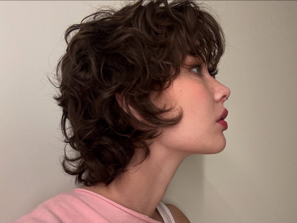 Short dark wavy pixie bob frames the face in side profile