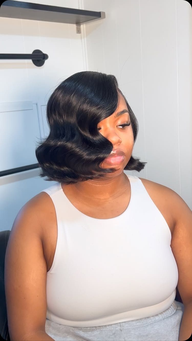 Woman wearing a glossy defined short wavy black bob with a side part